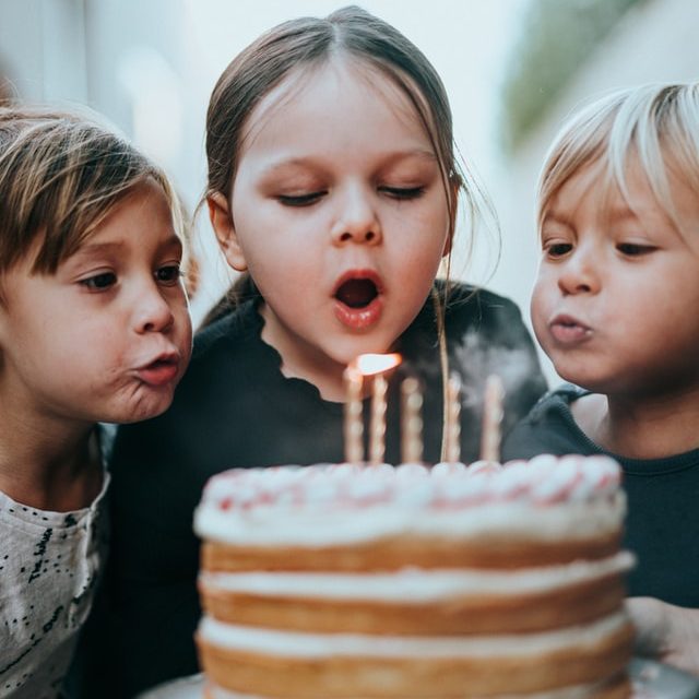 Girl blowing out candles on her birthday cake with two children helping